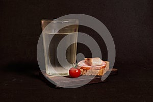 Faceted glass of vodka, sandwich with rye bread, herring, ham, tomato