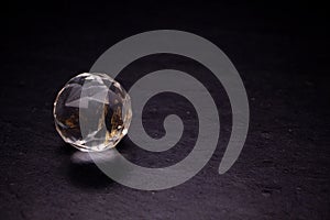 Faceted sphere, sparkling crystal on dark, black background. Large glass with light refraction, stone backdrop. Empty space for