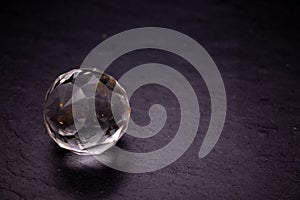 Faceted sphere, sparkling crystal on dark, black background. Large glass with light refraction, stone backdrop. Empty space for