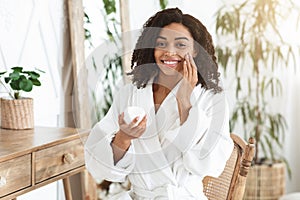 Facial Beauty Treatment. Attractive Black Woman Applying Moisturising Cream On Skin