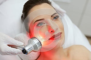 Facial Beauty Treatment. Woman Doing Red Led Light Therapy