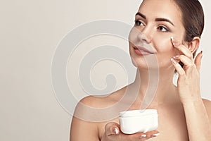 Facial Care. Female Applying Cream and Smiling. Portrait Of  Young Woman With Cosmetic Cream On Skin. Closeup Of Beautiful Girl Wi