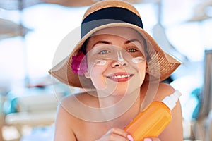 Facial Care. Young  Female Holding Bottle Sun Cream and  Applying on Face Smiling. Beauty Face.  Portrait Of Young Woman in hat Sm