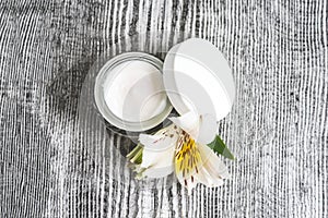 Facial cream and an alstroemeria flower on the wooden background.