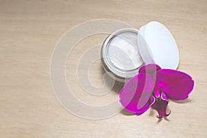 Facial cream and a flower on the wooden background