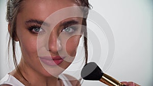 Facial Makeup. Woman putting blush with cosmetic brush closeup