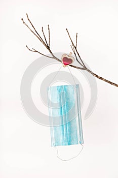 Facial mask against COVID19 coronavirus hangs on a bare branch of a tree for Valentine`s Day pinned down with a heart clothespin