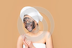 Facial mask. Skin care. Woman applying black clay mask isolated on beige studio background. Young spa model uses face