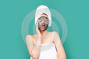 Facial mask. Skin care. Woman applying black clay mask isolated on blue studio background. Young spa model uses face