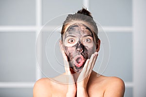 Facial mask. Skin care. Woman applying black clay mask isolated at home. Young spa model uses face care cream. Facial