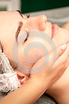 Facial massage. Hands of a masseur massaging neck of a young caucasian woman in a spa salon, the concept of health