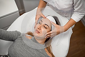 Facial massage for a woman in a sweater that lies on couch in a beauty salon