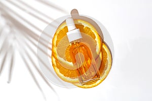 Facial oil dropper bottle with vitamin C on sliced orange with palm leaf shadow. Skin care concept