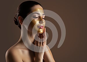 Facial peeling Golden Mask. Woman with Gold Lifting Face Mask over Dark Background. Beauty Model enjoying Skin Care Spa photo