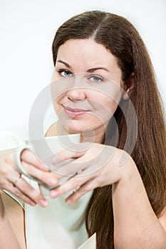 Facial portrait of young woman with tea mug in hands, grey background