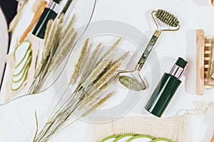 Facial roller from crystal rose quartz and massage tool jade on white background with dry flowers.