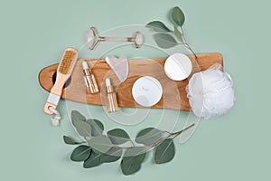 Facial roller, essential oils, cosmetic serums, face cream on green background with natural eucalyptus leaves. Beauty products,