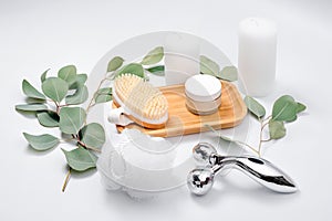 Facial roller, massage brush, face creme, washcloth and candles with natural eucalyptus leaves on light background. Beauty