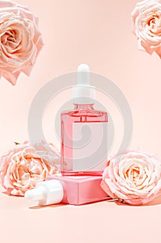 Facial serum in glass dropper bottle and pink roses on peach background. Natural skin care cosmetic. Beauty routine