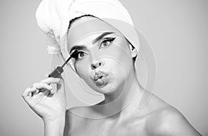 Facial treatment. Woman with towel on head applying black mascara on eyelashes with makeup brush. Brows coloring, wax photo