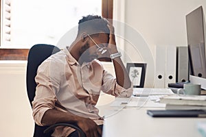 Facing a tough challenge in his workday. Shot of a young businessman looking tired while working in an office.