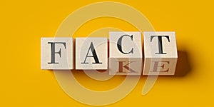 Fact and fake written on wooden blocks half flipped on yellow background, false and true, propaganda or news information concept