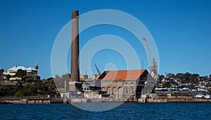 Factory brick smoke stack at historic dockyard and boat storage with crane against blue sky set on Cockatoo Island Sydney Harbour