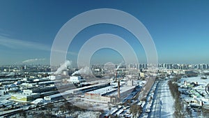 Factory buildings covered with snow. Factory smoke chimneys. There is a railway nearby. You can see the city blocks. Winter