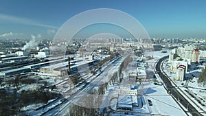 Factory buildings covered with snow. Factory smoke chimneys. There is a railway nearby. You can see the city blocks. Winter