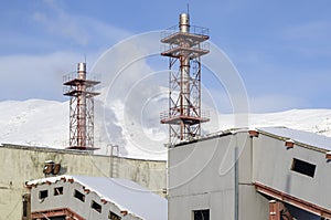 Factory buildings and two chimneys against the background of snowy mountains and blue sky