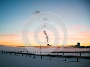 Factory chimney smoke on horizon, distant winter landscape