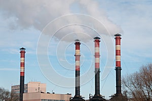 Factory chimneys emit puffs of smoke against the blue sky.