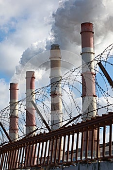 Factory chimneys smoke behind a fence with barbed wire