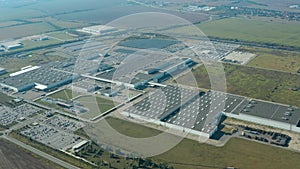 Factory on green field in europe. View from above on industrial territory and many cars nearby. White trucks on the parking zone.