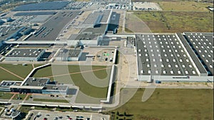 Factory on green field in europe. View from above on industrial territory and many cars nearby. White trucks on the parking zone.