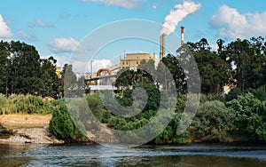 Factory next to river emiting plumes of smoke