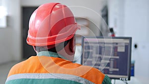 Factory operator in a helmet at work near computer