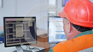Factory operator in a helmet at work near computer