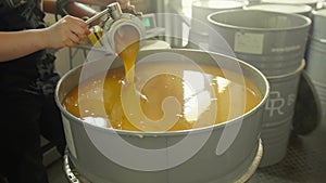 Factory worker feeling a barrel with homogenized honey with many barrels on the background