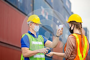 Factory worker man checking fever by digital thermometer for scan and protect from Coronavirus COVID-19 at cargo containers -