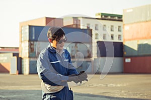 Factory worker man in sunglasses wearing gloves and holding hard hat at cargo container
