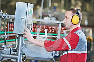 Factory worker operating conveyor with beer beverage bottles moving