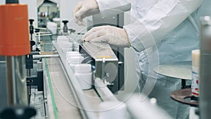 Factory worker is regulating a conveyor with pill tubs