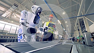 Factory worker is regulating robot`s settings by remote control during working process