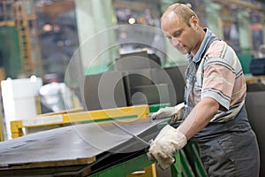 Factory worker removing metal burrs from steel sheet