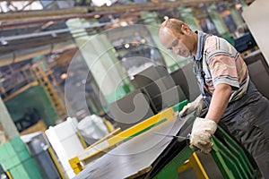 Factory worker removing metal burrs from steel sheet