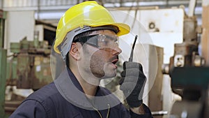 Factory worker talking on portable radio while inspecting machinery parts