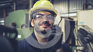Factory worker talking on portable radio while inspecting machinery parts