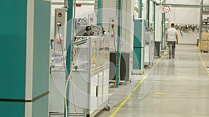 Factory worker walking by modern injection moulding machines lined up one behind the other