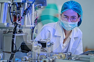 Factory worker woman with gown uniform stand near part of mask producing machine and look at camera with smiling under hygiene